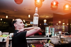 Barman hold bottle on elbows of hand at the bar