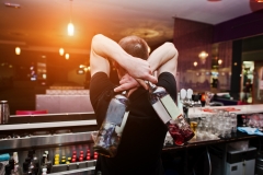 Young barman holding bottles for coctail at the bar