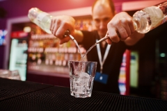 Barman hold bottle and pouring cocktail at the bar