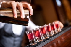 close-up of barman hand pouring alcohol into shot glasses in a n